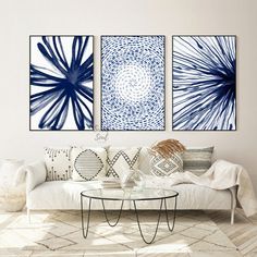 three blue and white paintings on the wall above a couch in a living room with pillows