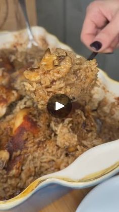 a person holding a spoon in a bowl full of food with rice and meat on it