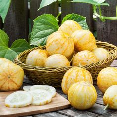 a basket filled with cucumbers sitting on top of a wooden table next to green leaves