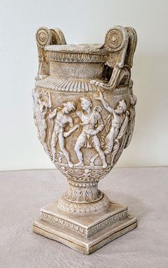 an antique vase with figures on it sitting on a table next to a white wall