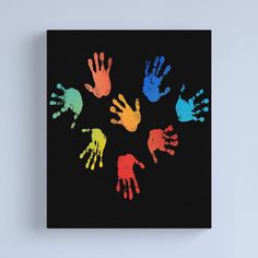 multicolored handprints on black canvas mounted on wall with white frame and blue background