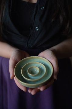 a woman holding a green bowl in her hands with a spiral design on the bottom