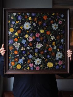 a person holding up a framed painting with flowers on it