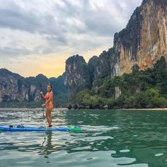 a woman paddle boarding on the water in front of some mountains and cliffs at sunset