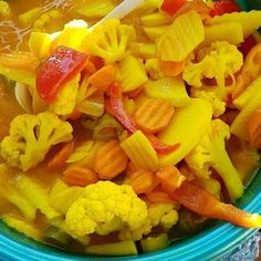 a blue bowl filled with lots of different types of vegetables and fruit in liquid next to a spoon