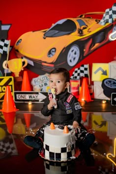 a young boy sitting on top of a cake in front of a race car backdrop