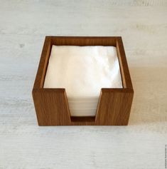 an empty napkin holder on top of a wooden table with white linen in the middle