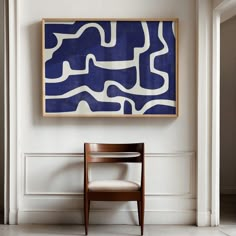 a chair sitting in front of a blue and white painting hanging on the side of a wall