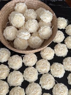 a bowl filled with white frosted roses on top of a black table next to other cupcakes