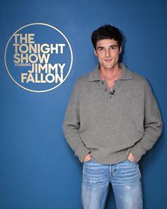 a man standing in front of a blue wall with the tonight show logo on it