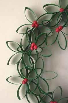 a paper wreath with red berries and green leaves on the front, hanging from a wall