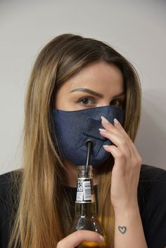 a woman wearing a face mask and holding a beer in front of her face while covering her mouth