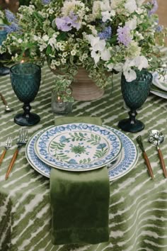 the table is set with green and white plates, silverware, and floral centerpieces