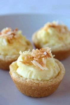 three small cupcakes with coconut toppings on a white plate in front of the camera