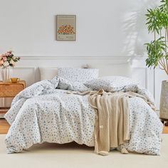 a bed with blue and white flowers on it in a room next to a potted plant