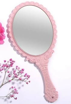 a pink mirror sitting on top of a table next to flowers