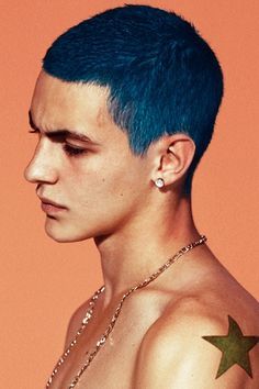 a young man with blue hair and piercings on his chest wearing a star necklace