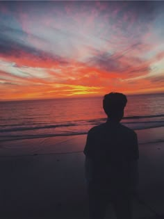 a man standing on top of a beach next to the ocean under a colorful sky