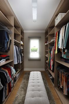 a walk - in closet with lots of clothes on the shelves and a white bench