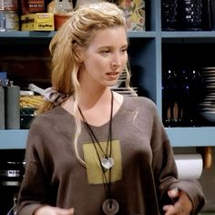 a woman standing in front of a blue book shelf holding a cell phone and wearing a necklace