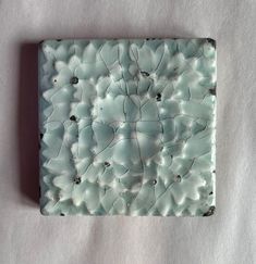 a square piece of art made out of white and blue glass with small holes in the middle