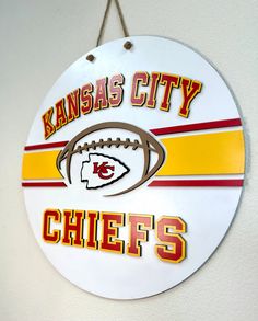 kansas city chiefs football sign hanging on the side of a white wall with red and yellow stripes