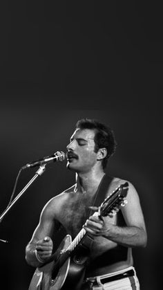 a shirtless man holding a guitar and singing into a microphone while standing on stage