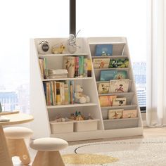 a white book shelf filled with books in a living room next to a large window