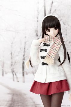 a doll is standing in the snow wearing a white sweater and red skirt with a scarf around her neck