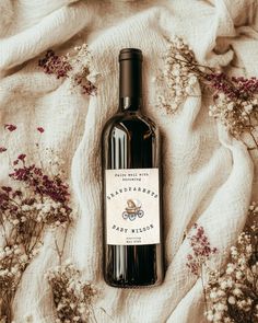 a bottle of wine sitting on top of a blanket next to dried plants and flowers