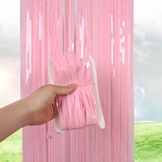 a hand holding a pink piece of paper in front of a wall with white strips on it