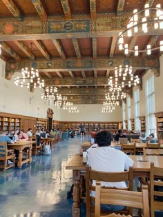 people are sitting at tables and reading books in a large room with high ceiling lights