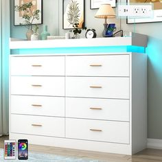 there is a white dresser with blue lights on it and pictures hanging above the drawers