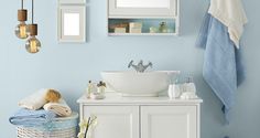 a white sink sitting under a bathroom mirror next to a basket filled with flowers and towels