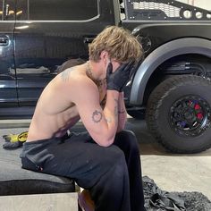 a shirtless man sitting on top of a bench next to a large black truck