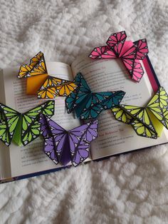 several colorful butterflies are on top of an open book, which is sitting on a white blanket