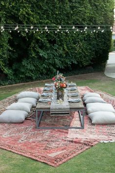 an outdoor dining table with pillows on it and lights strung over the tables in the background