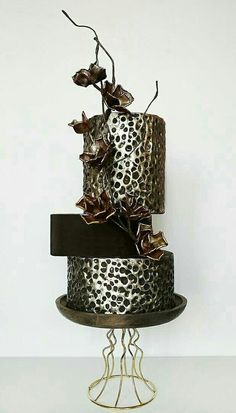 a three tiered cake decorated with leopard print and metal flowers on a stand in front of a white wall