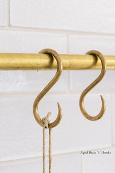 two brass hooks hang from a metal bar against a white brick wall with gold colored handles