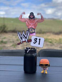 a toy wrestler standing on top of a table next to a black trash can and a sign