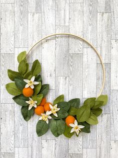 an orange wreath with white flowers and green leaves on a wood floor, ready to be decorated