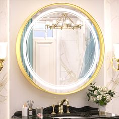 a bathroom vanity with a round mirror above it and flowers in vases on the counter