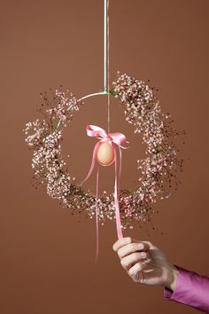 a hand holding a pink ribbon around a wreath ornament with eggs in it