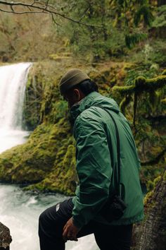 a man sitting on a rock looking at a waterfall