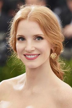 a woman with red hair wearing a strapless dress and gold earrings, posing for the camera