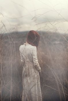 a woman standing in tall grass with her back to the camera