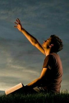 a man sitting in the grass reaching up to catch a frisbee