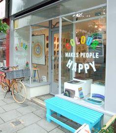 there is a blue bench in front of the storefront that says make people happy