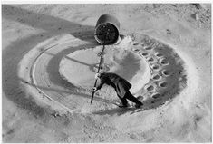 a man walking in the sand next to a large metal object with wheels on it