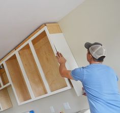 a man in blue shirt and cap painting cabinets with white paint on the wall behind him